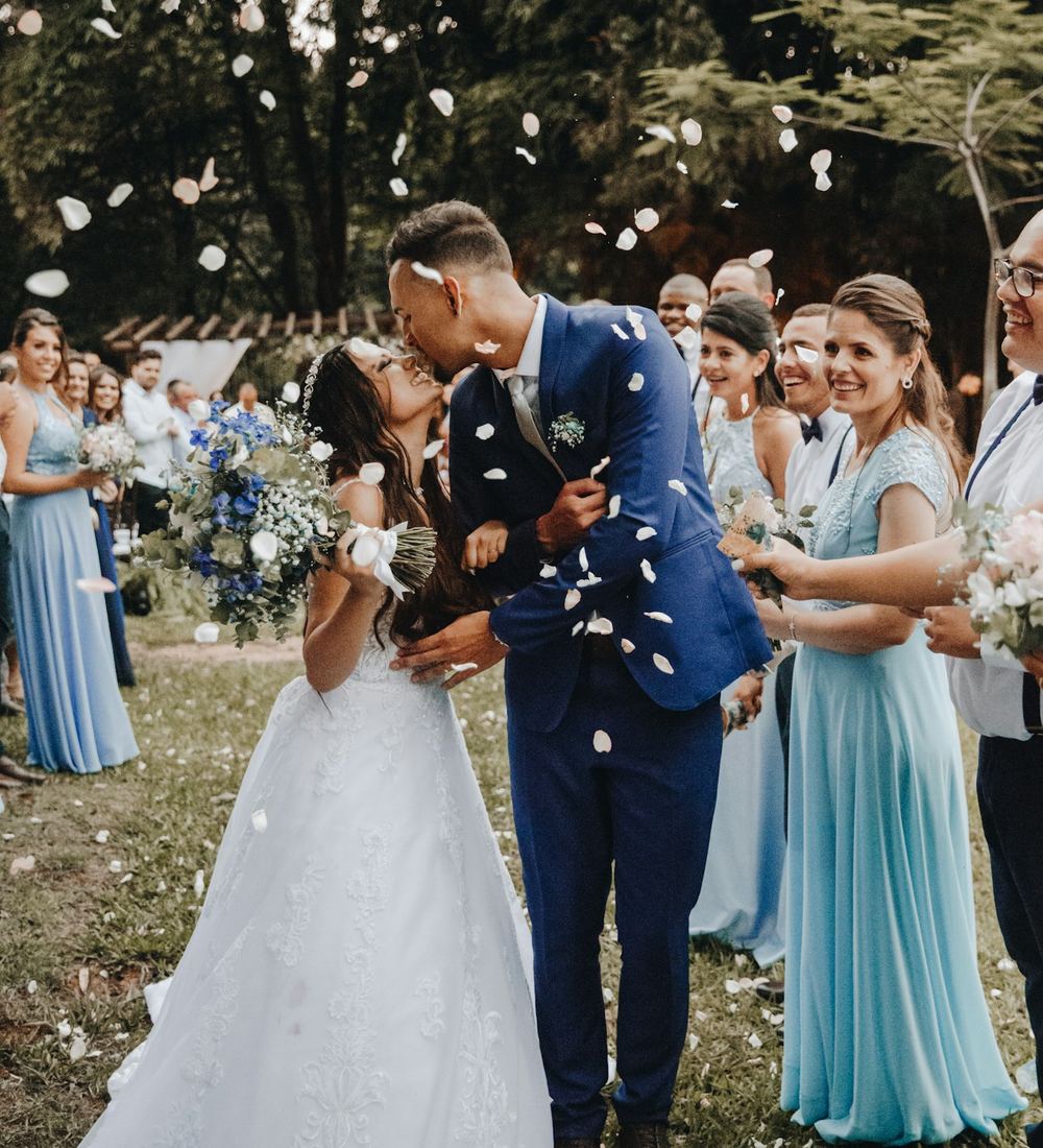 A couple kissing at their outdoor wedding while guests celebrate